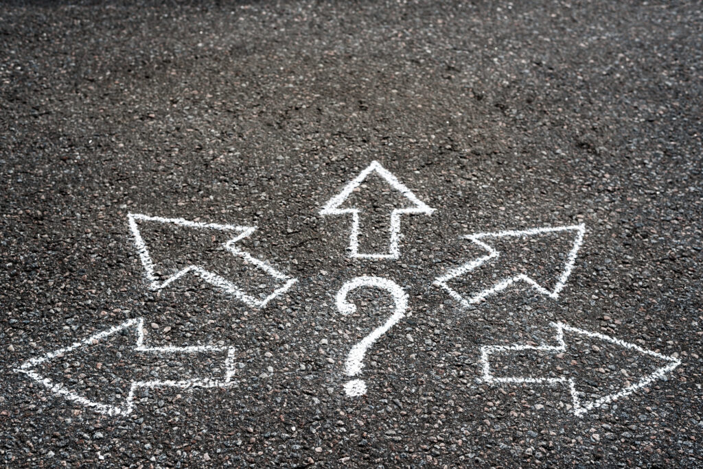 Bild von einem mit Kreide auf Asphalt gemalten Fragezeichen, um das 5 Pfeile platziert sind, die weg zeigen.