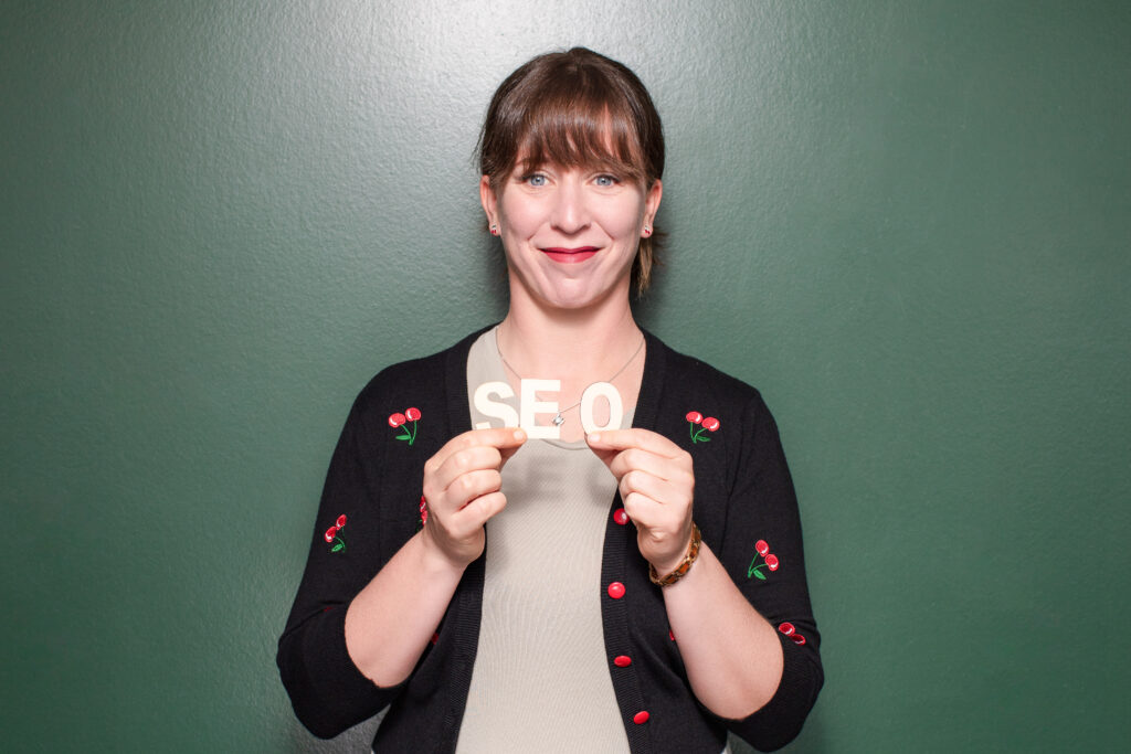 Bild von Nina Kirsch, Gründerin von kirschwerk GmbH, vor einem grünen Hintergrund. Sie lächelt und hält die Buchstaben "SEO" in den Händen.