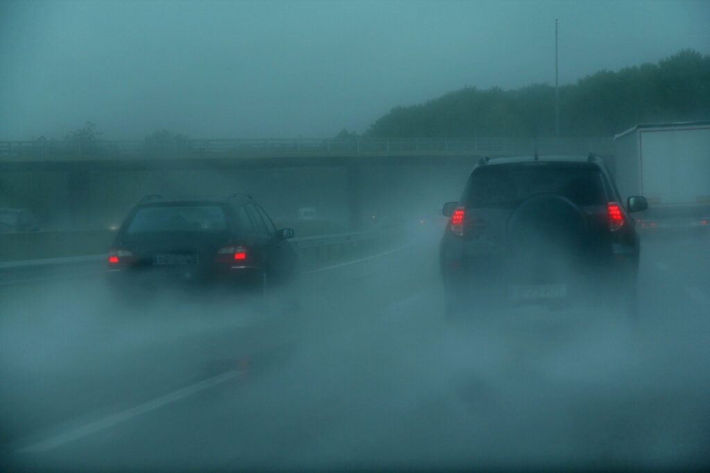 Bild einer Fahrt auf einer äußerst verregneten Autobahn. Zwei schwarze Autos fahren vorraus.