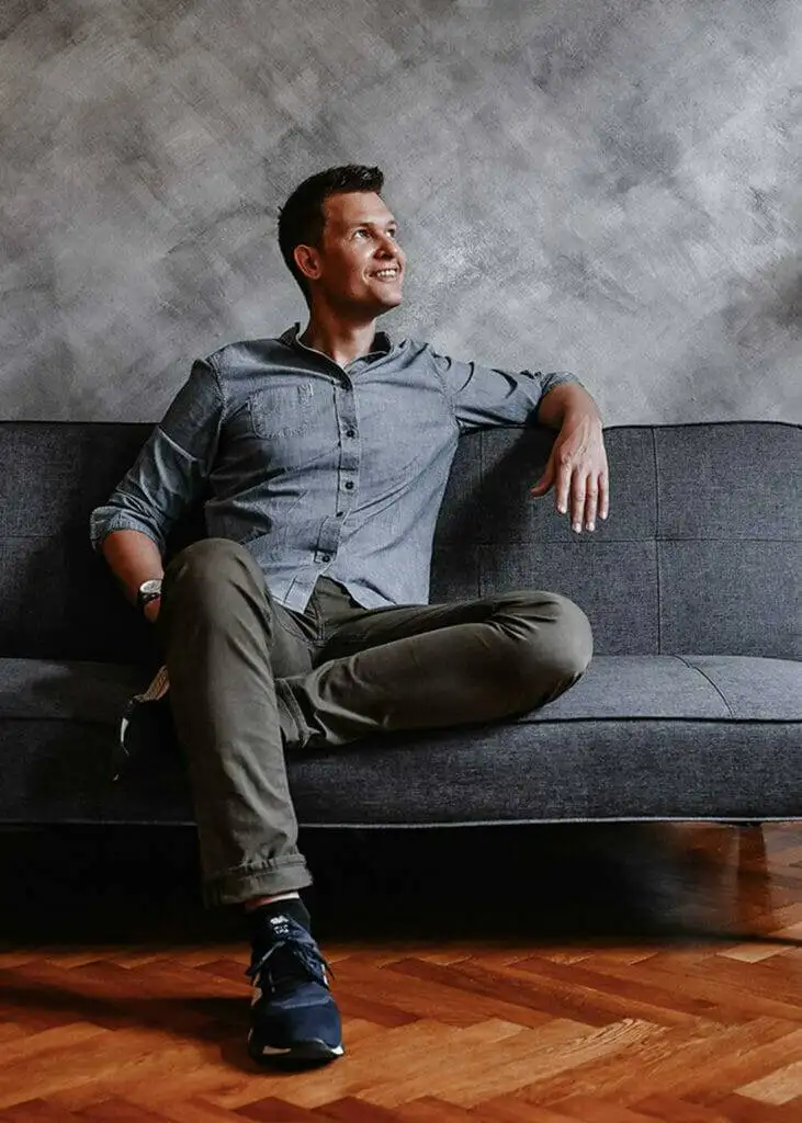 Bild von Martin Wetzel, Inhaber von Martin Wetzel Design. Er hat kurzes dunkles Haar, sitzt lässig auf einer Couch und lächelt.