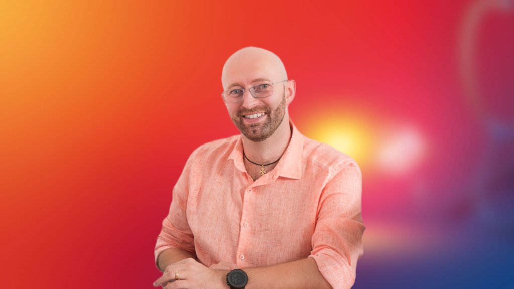 Porträtfoto von Julian Hofmann, dem Gründer von JHS Marketing. Er sitzt freundlich lächelnd vor einem farbenfrohen Hintergrund.